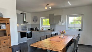 A modern kitchen with white cabinets, a wooden dining table, and grey chairs. - Familienfreundliches Ferienhaus (Oldenburg in Holstein)