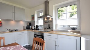 A modern kitchen with white cabinets, a stainless steel range hood, a microwave, a coffee maker, and a window with a view of greenery. - Familienfreundliches Ferienhaus (Oldenburg in Holstein)