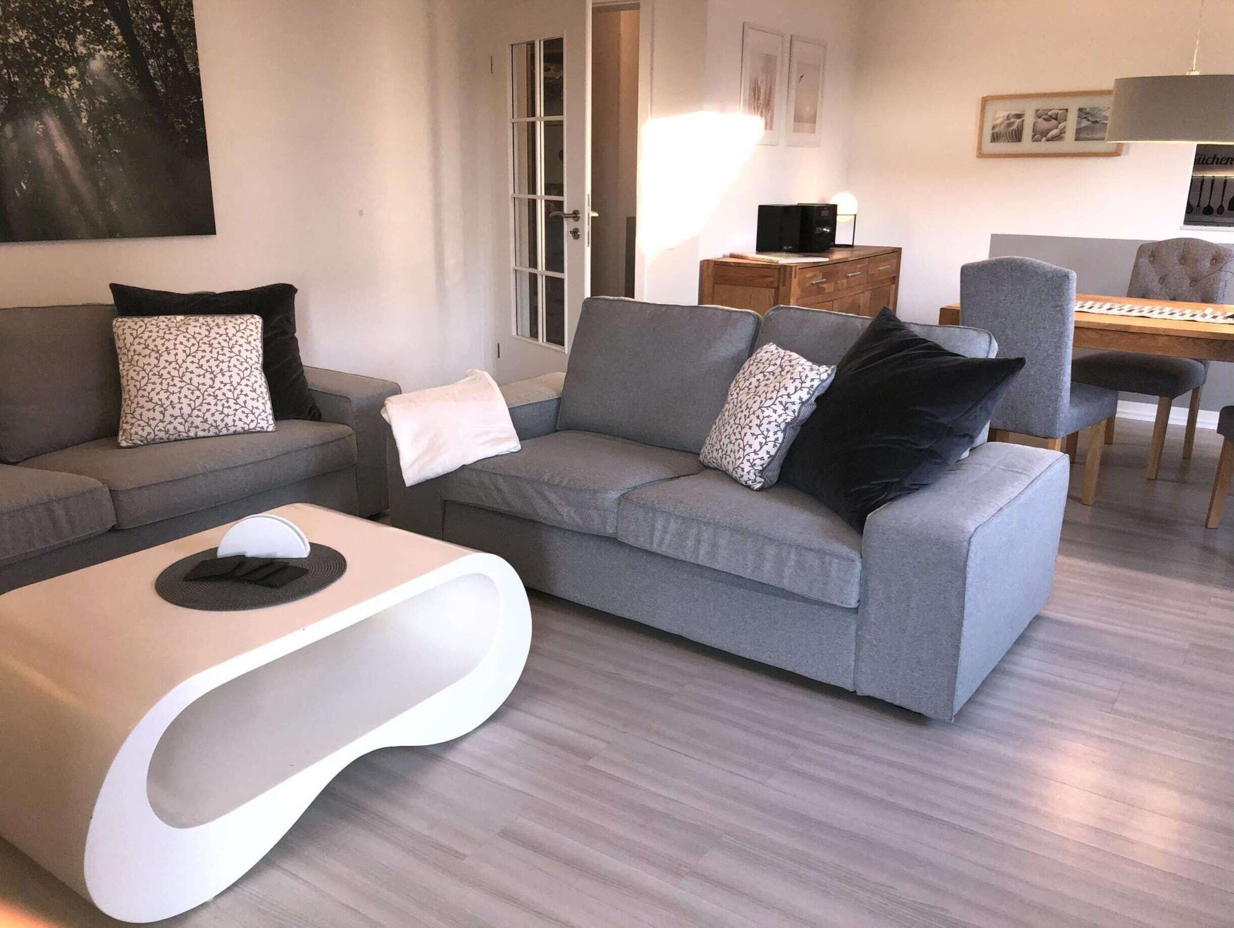 A modern living room with a grey sofa, a white coffee table, and a dining area with a wooden table and chairs.