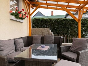 An outdoor patio with wicker furniture, a glass table, and a flower box with red and pink flowers. - Ferienhaus mit Kamin in Thale-friedrichsbrunn (Thale)