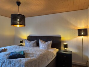 A bedroom with a bed, two bedside lamps, a nightstand, and a ceiling light fixture. - Ferienhaus mit Kamin in Thale-friedrichsbrunn (Thale)