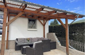 A covered outdoor seating area with a sofa and table, wooden pergola structure, and a stone wall. - Ferienhaus mit Kamin in Thale-friedrichsbrunn (Thale)