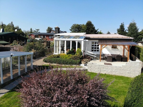 A house with a conservatory, a patio with outdoor furniture, and a garden with purple-leaved shrubs. - Ferienhaus mit Kamin in Thale-friedrichsbrunn (Thale)