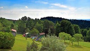 A park with playground equipment, a small building, and a forested hill in the background. - Alpine View Wellness Escape (Waldkirchen)