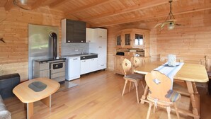 A wooden cabin interior with a kitchen, dining area, and a sofa. - Alpine View Wellness Escape (Waldkirchen)