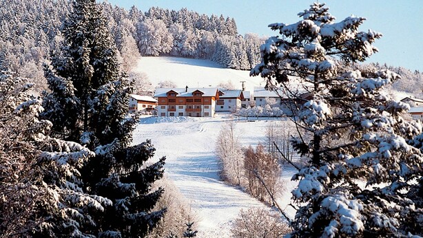 A snow-covered landscape with a building featuring multiple windows and a sloped roof. - Alpine View Wellness Escape (Waldkirchen)