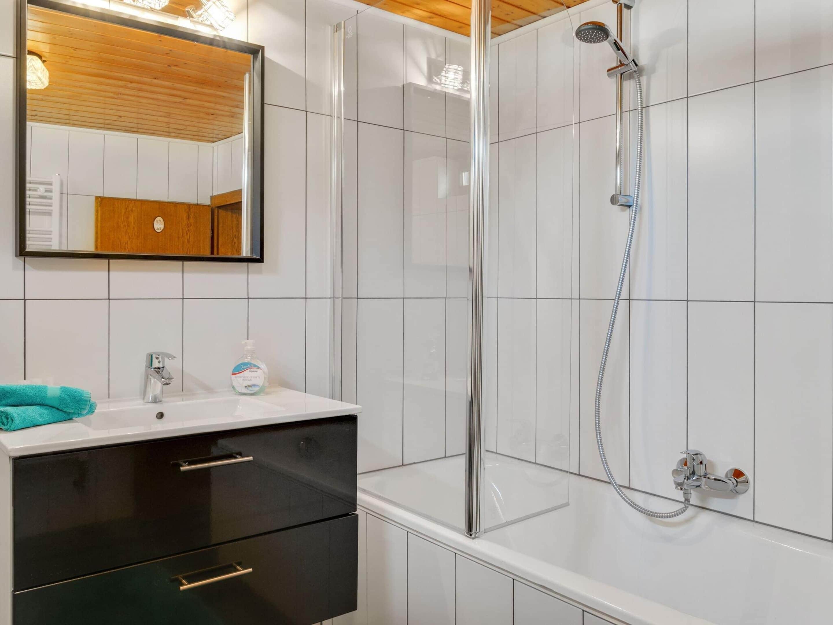 A modern bathroom with a glass-enclosed shower, a white sink with a mirror above it, and black cabinets below.