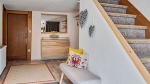 Un interior moderno con una escalera de madera, un banco, un espejo y un aparador.