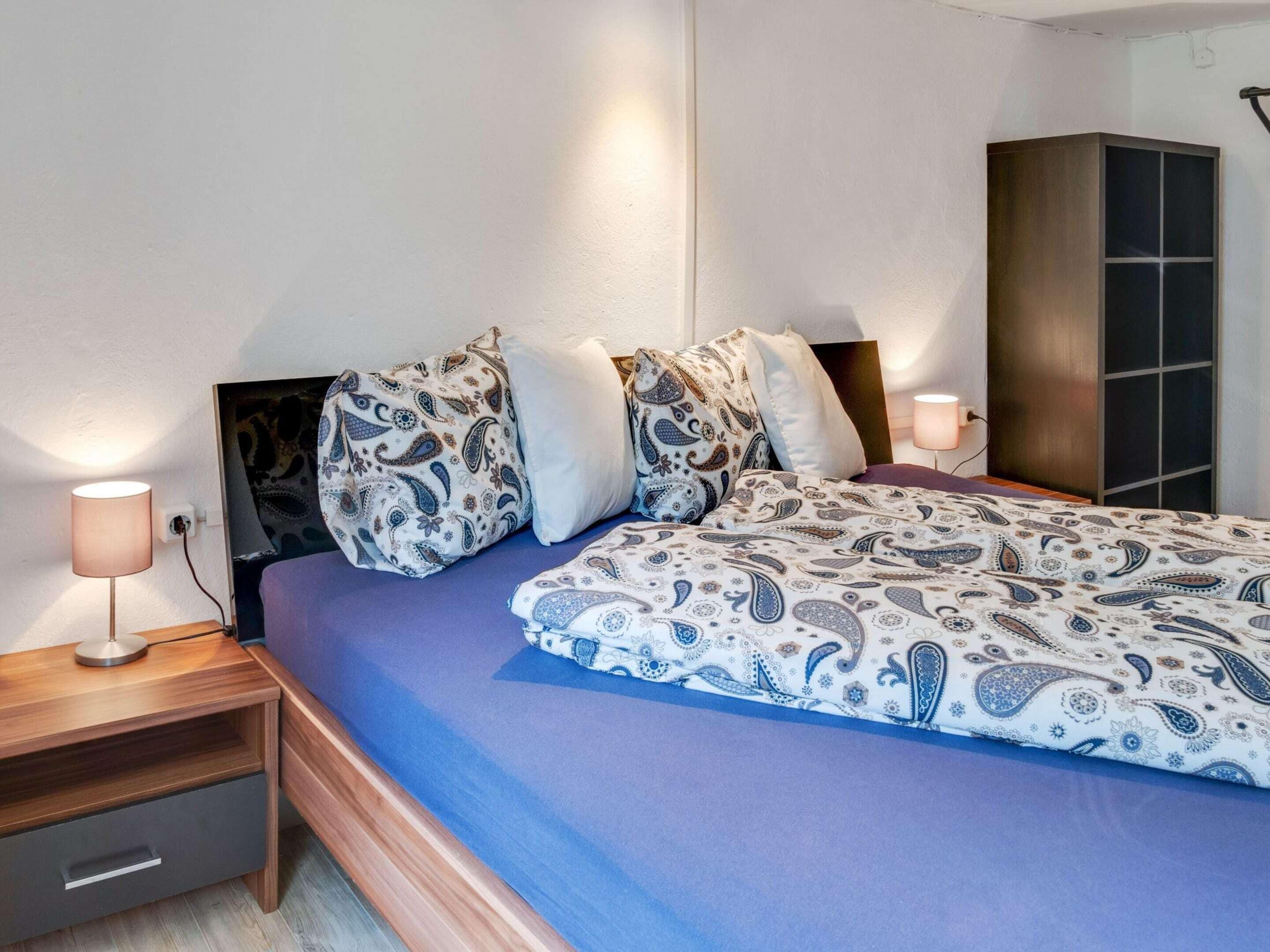 Un dormitorio con cama, mesitas de noche, lámpara y armario.