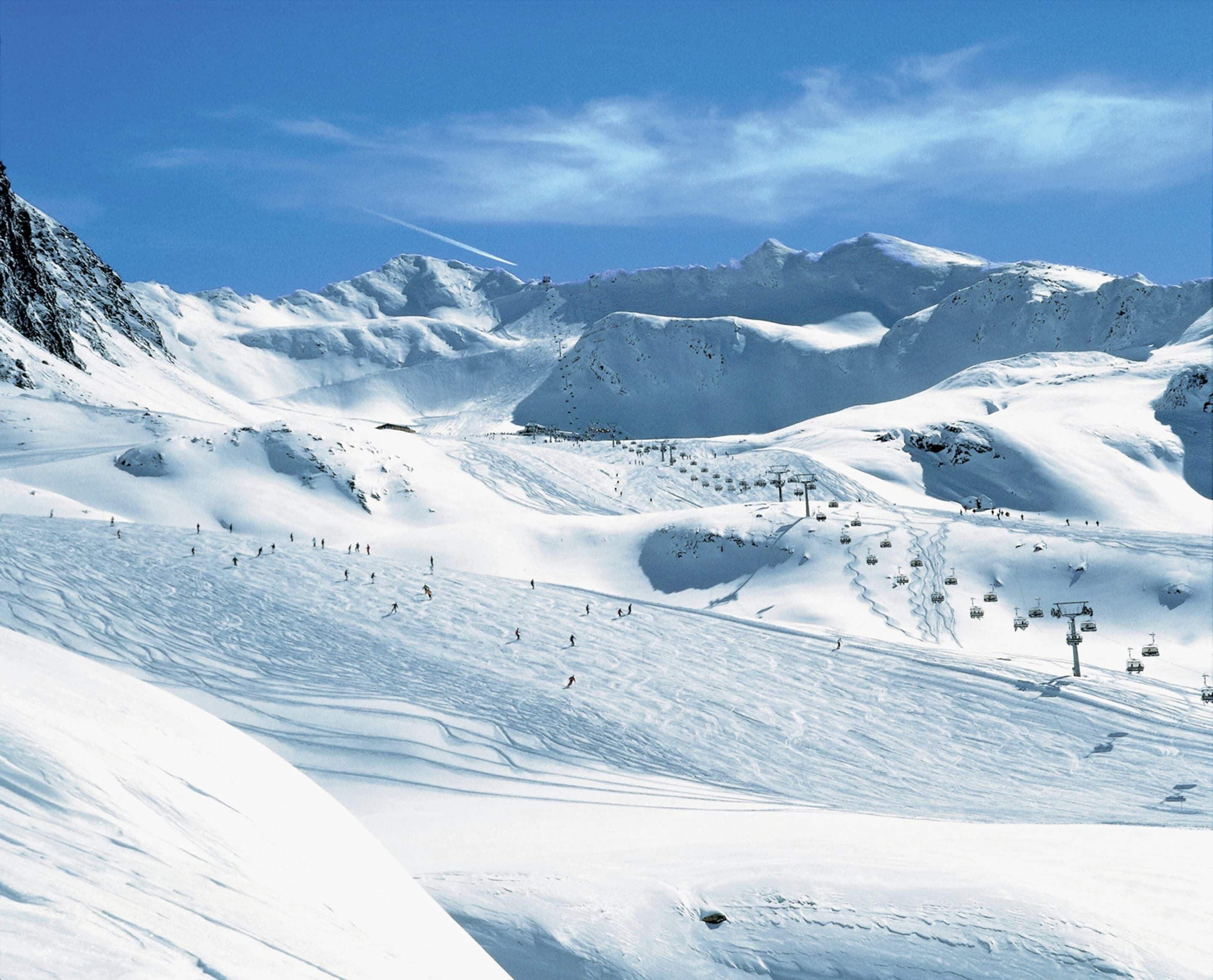 Encosta de montanha coberta de neve, com teleféricos e esquiadores.