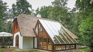 A house with a thatched roof, large glass windows, and a stone pathway leading to the entrance. - Ferienhaus Boschhuys (Uelsen)