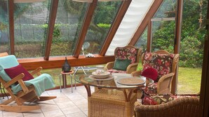 A conservatory with wicker furniture, a glass table, and a view of greenery. - Ferienhaus Boschhuys (Uelsen)
