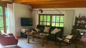 A cozy living room with a green sofa, a red armchair, a wooden coffee table, and a television. - Ferienhaus Boschhuys (Uelsen)