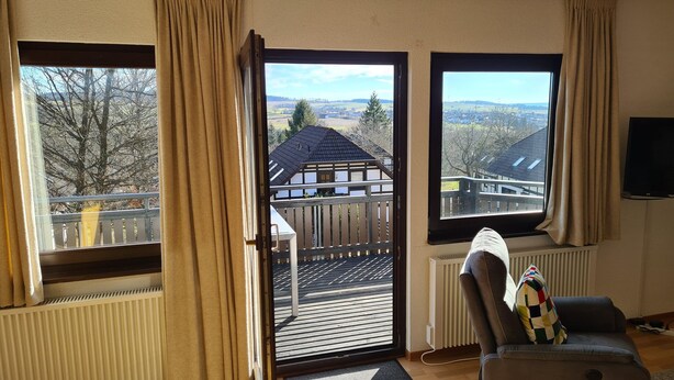 A living room with a view of a house and trees through open doors. - Chalet in Frankenau Nahe Skipisten & Edersee (Frankenau)