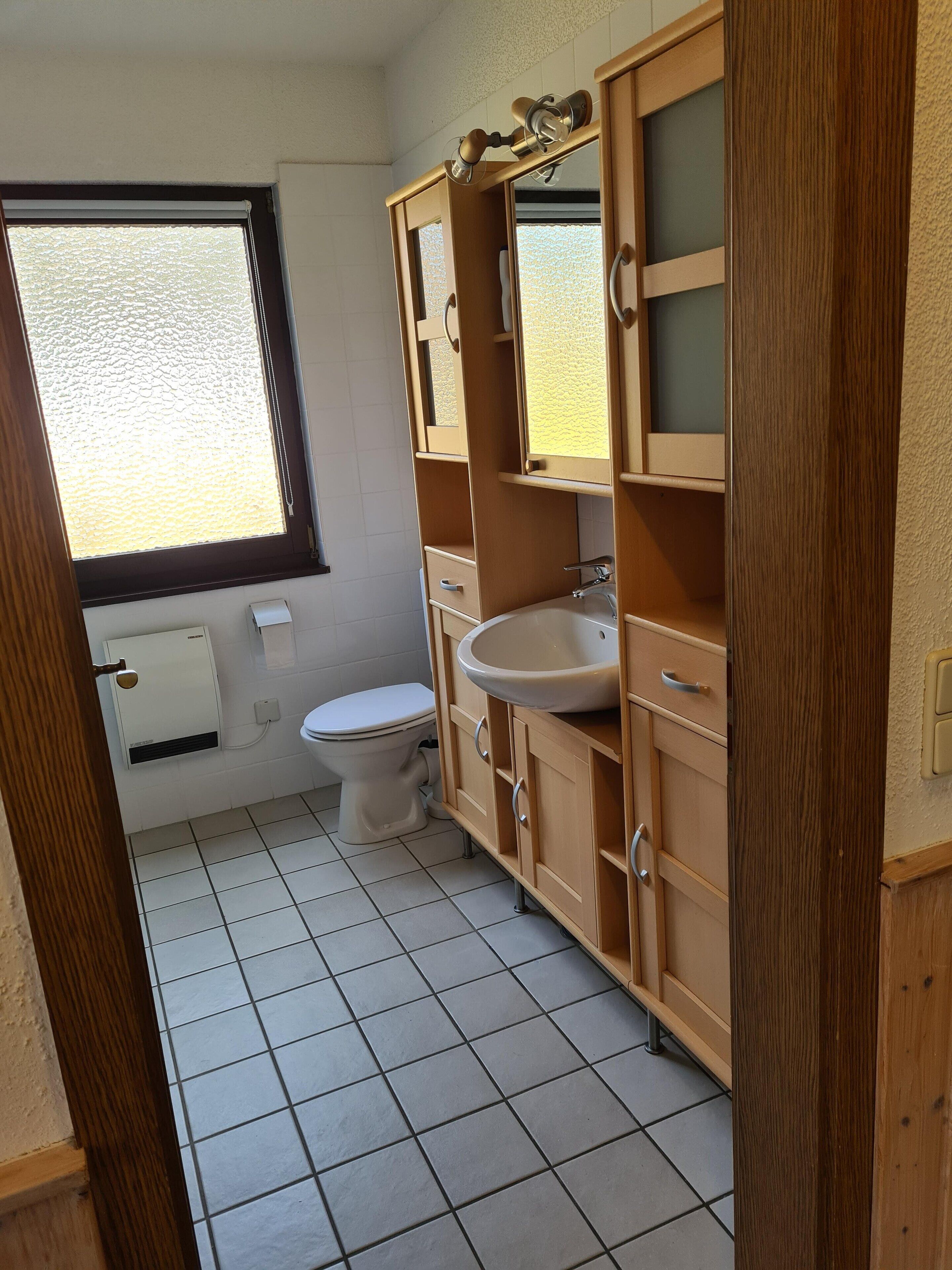 Een kleine badkamer met toilet, wastafel en houten kastjes.