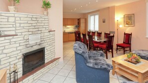 Ein Wohnzimmer mit Kamin aus Stein, ein Essbereich mit roten Stühlen und eine Küche im Hintergrund.