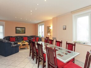 A dining area with a glass table and wooden chairs, a sofa with red cushions, and a painting on the wall.