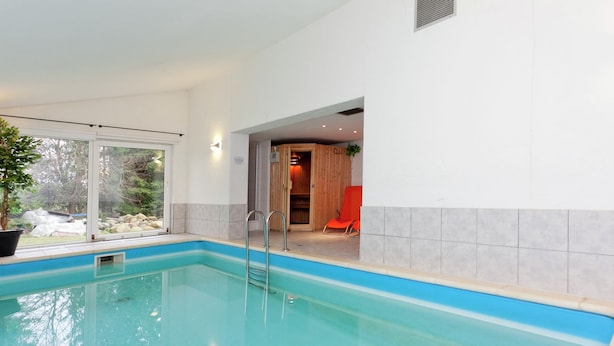 Ein Schwimmbecken mit klarem, blauem Wasser, einer Holzterrasse und Blick ins Freie durch große Fenster.