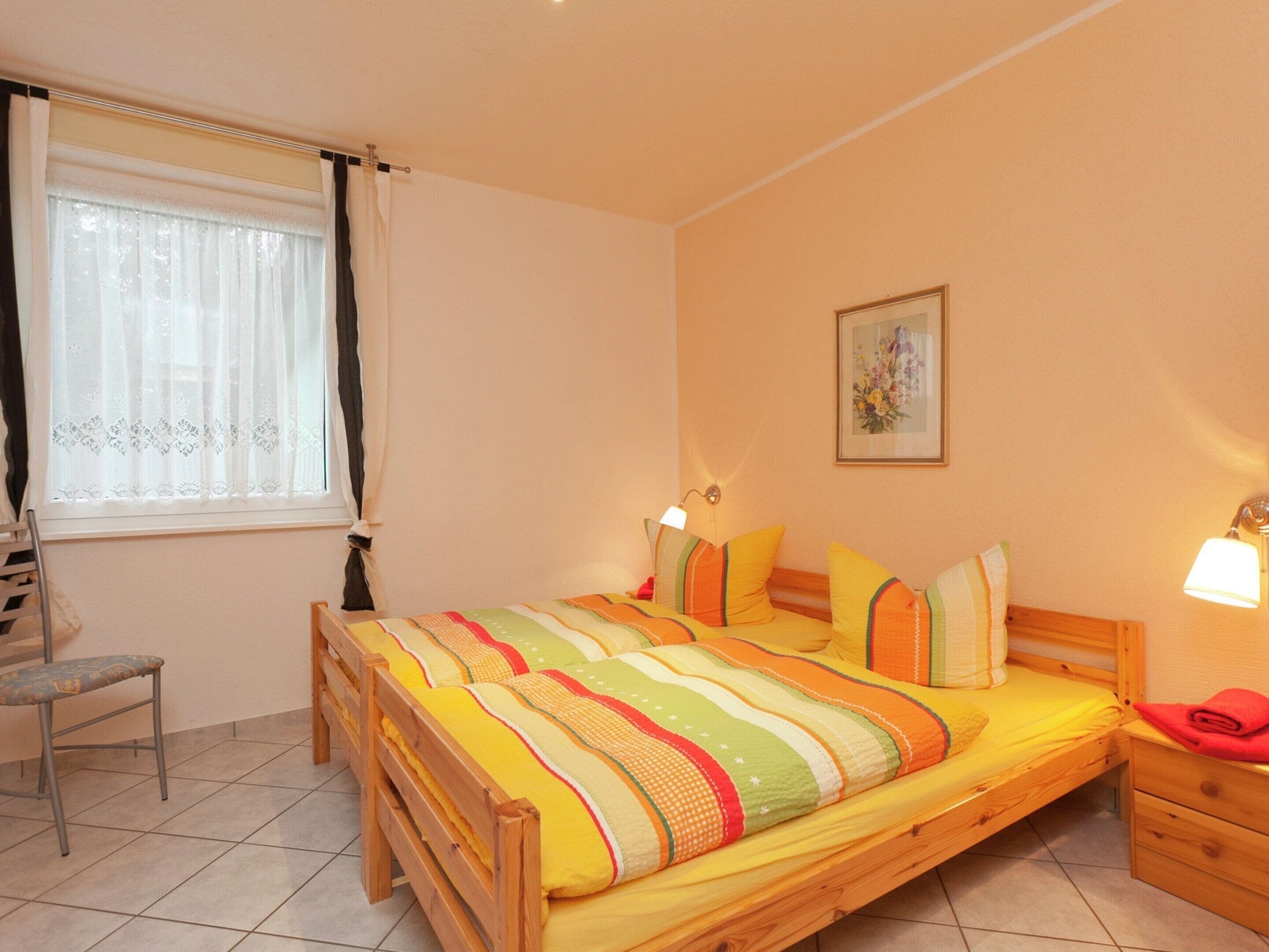 Ein Schlafzimmer mit einem hölzernen Bett, einem Stuhl, einem Nachttisch und einem Fenster mit Vorhängen.