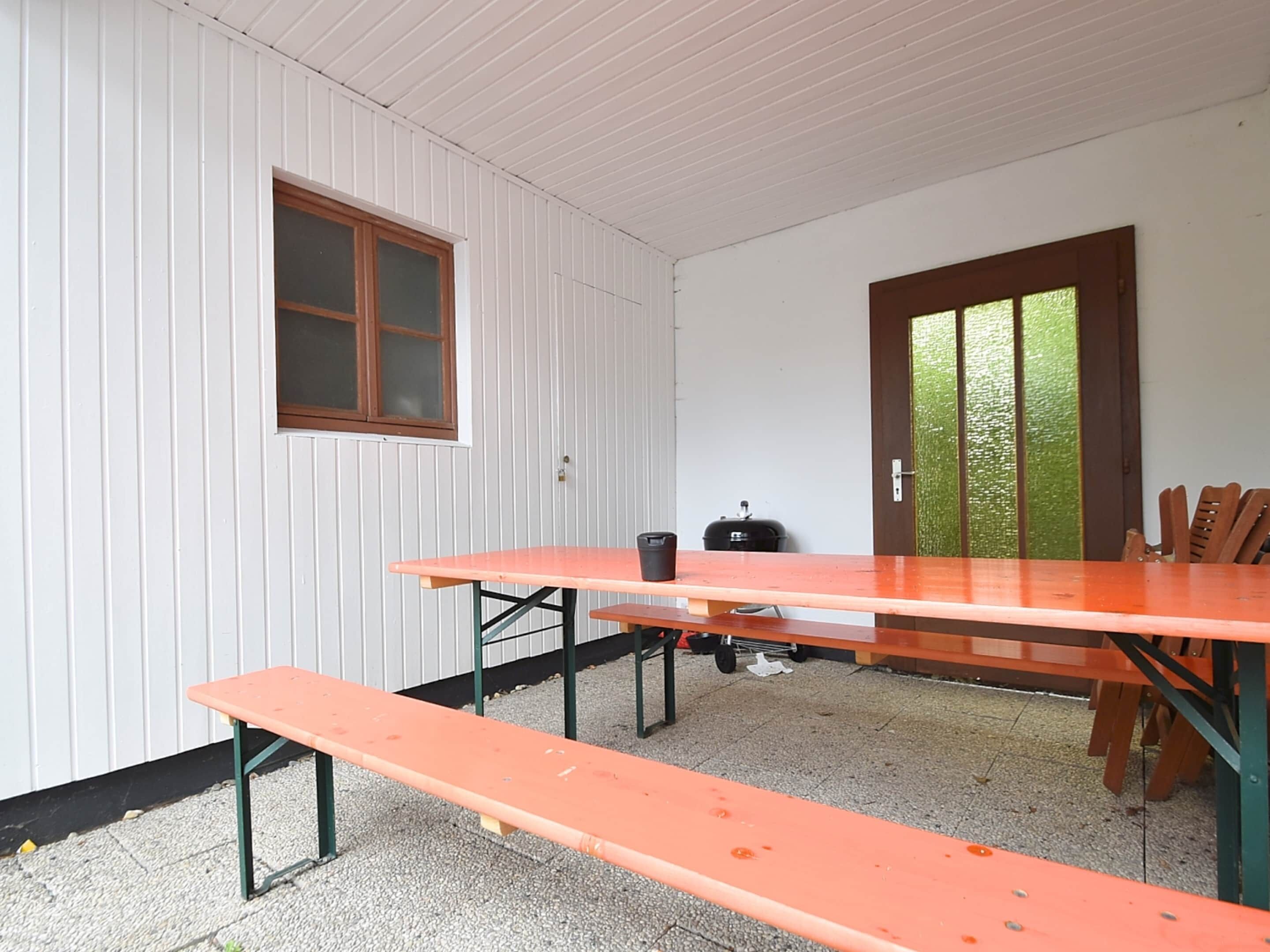 A room with a wooden table and benches, a window, and a door.