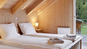 Une chambre dans une cabane en bois, avec deux lits, une table de chevet et une fenêtre donnant sur un jardin.