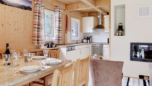 Une charmante cabane en bois comprenant un coin repas, une cuisine et un téléviseur fixé au mur.