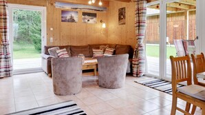 Un salon chaleureux avec un décor intérieur en bois, un canapé, deux fauteuils, une table basse et un coin repas avec des chaises.