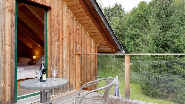 Une cabane en bois dotée d’un balcon, d’un lit et d’une table avec des chaises.