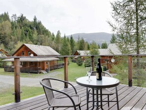 A wooden deck with a table and chairs, overlooking a forested area with cabins. - Delightful Chalet in Stadl an der Mur Styria near Ski Area (Stadl-Predlitz)