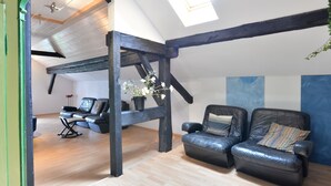 Une pièce de style « loft », avec des poutres en bois apparentes, une lucarne et un coin salon doté de canapés en cuir.