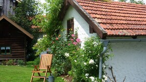 Un chalet rustique en bois, avec un toit recouvert de tuiles rouges, entouré d’une végétation luxuriante et de plantes en fleurs.
