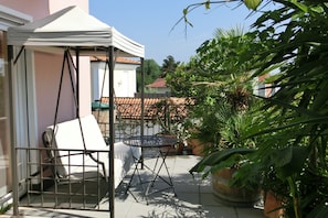Un espace extérieur abrité, avec une table et des chaises en métal, entouré de plantes en pot et d’une structure en forme de tente blanche.