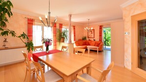 A spacious dining area with a wooden table and chairs, a chandelier, and a sofa in the background. - Apartment in Bavaria With Scenic Garden Views (Deggendorf)
