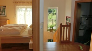 A bedroom with a bed, a window with curtains, a wooden staircase, and a bathroom visible through an open door. - Apartment in Bavaria With Scenic Garden Views (Deggendorf)
