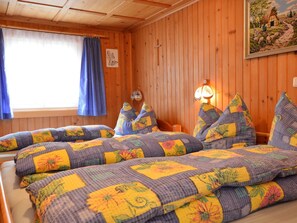 Une pièce chaleureuse aux murs en bois, un lit recouvert d’une literie à motifs floraux, une fenêtre ornée de rideaux bleus et une lampe fixée au mur.