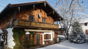 A wooden chalet with a balcony, a wooden staircase, and a snow-covered garden. - Spacious Apartment in Steingaden near Ski Area (Steingaden)