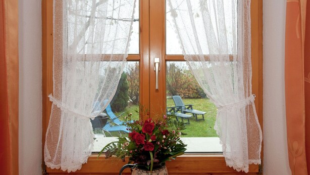 A window with lace curtains, a wooden floor, and a vase with flowers. - Spacious Apartment in Steingaden near Ski Area (Steingaden)