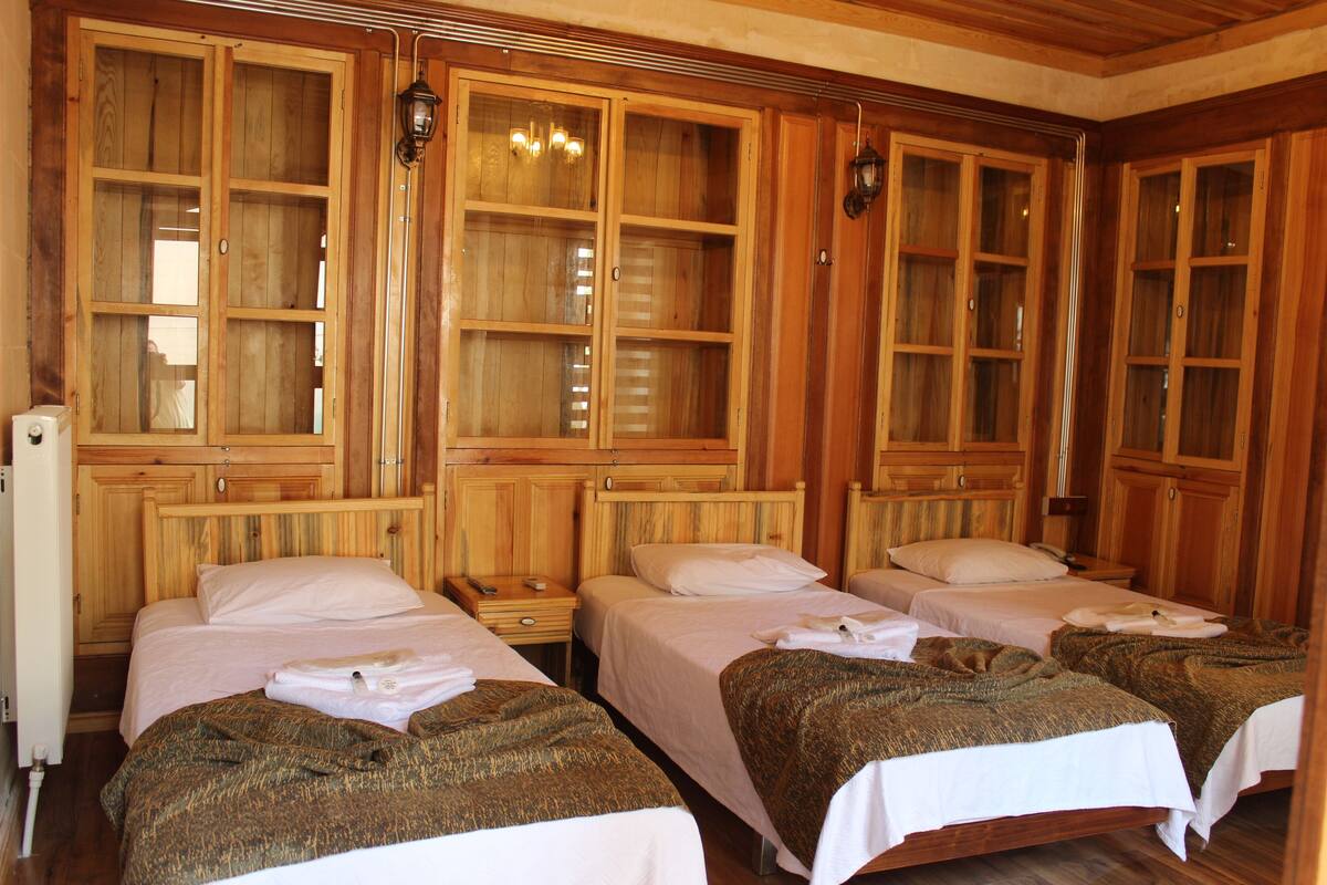 Une chambre d’hôtel avec quatre lits simples, des armoires en bois et une grande fenêtre.