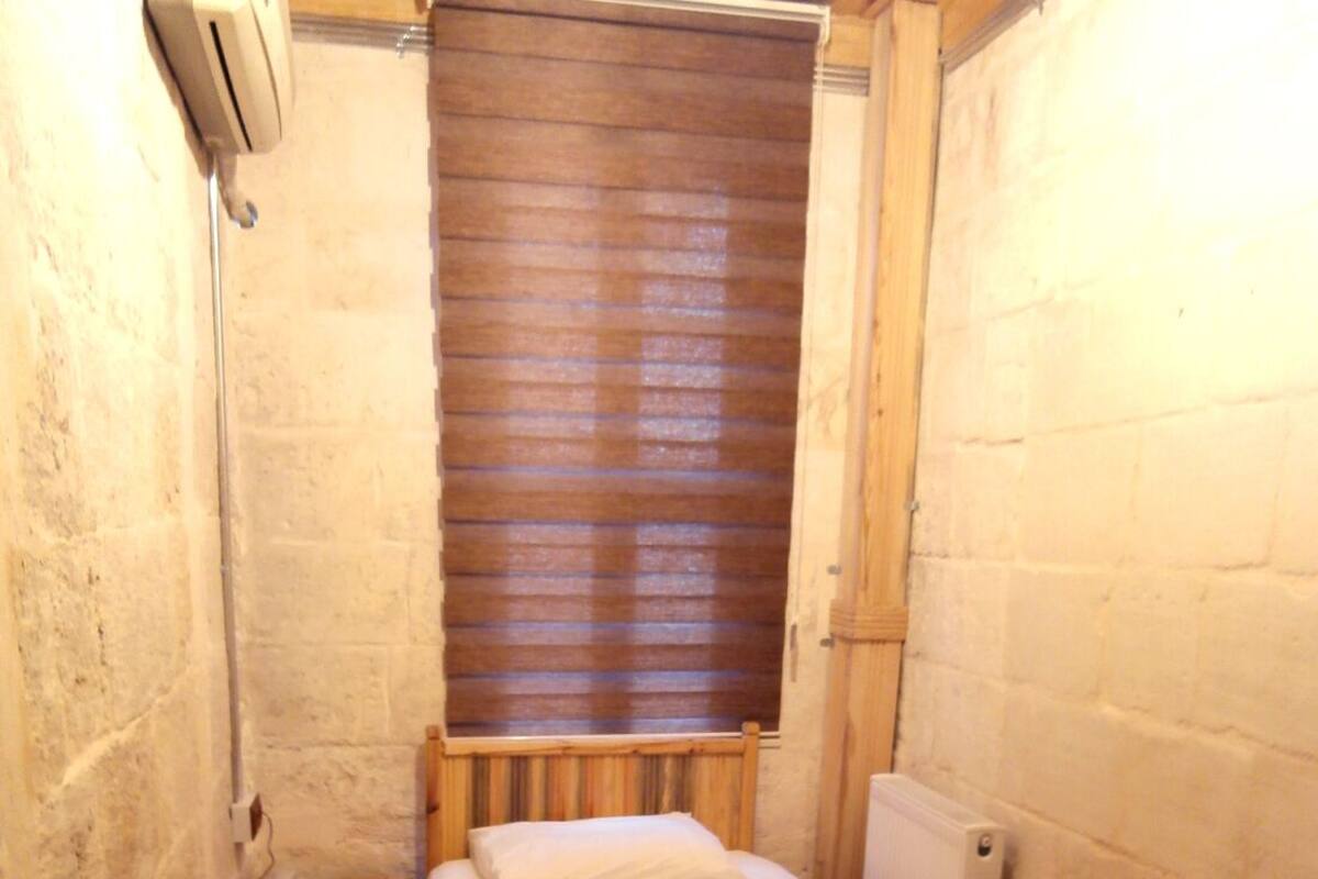 Une petite pièce étroite, avec un lit en bois, une table de chevet sur laquelle se trouve un téléphone et un radiateur.