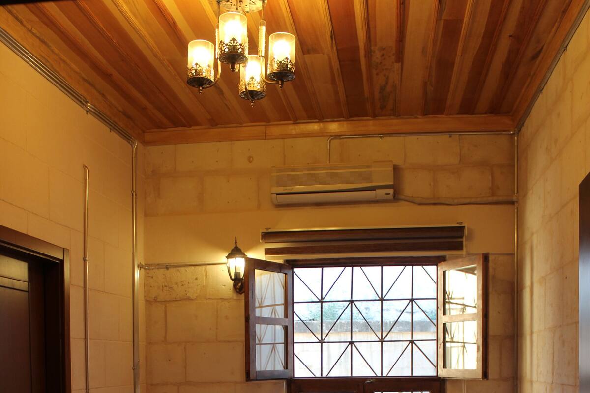 Une chambre avec un plafond en bois, une grande fenêtre offrant une belle vue, un lit avec du linge de lit blanc et une table de chevet avec une lampe.