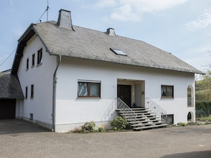 A two-story house with a sloped roof, a front entrance with steps, and a small porch area.