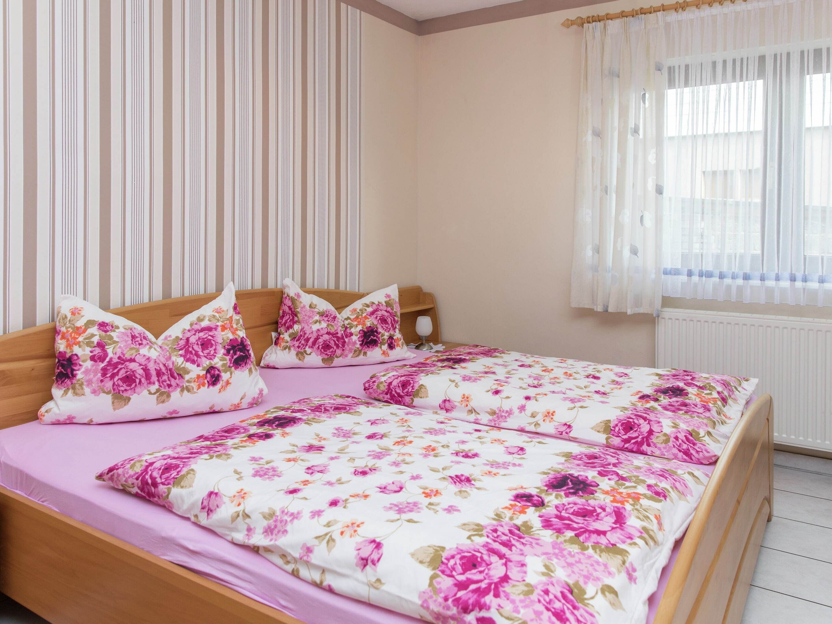 Un dormitorio con cama, ropa de cama floral, cortinas y una ventana.