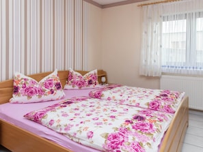 A bedroom with a bed, floral bedding, curtains, and a window.