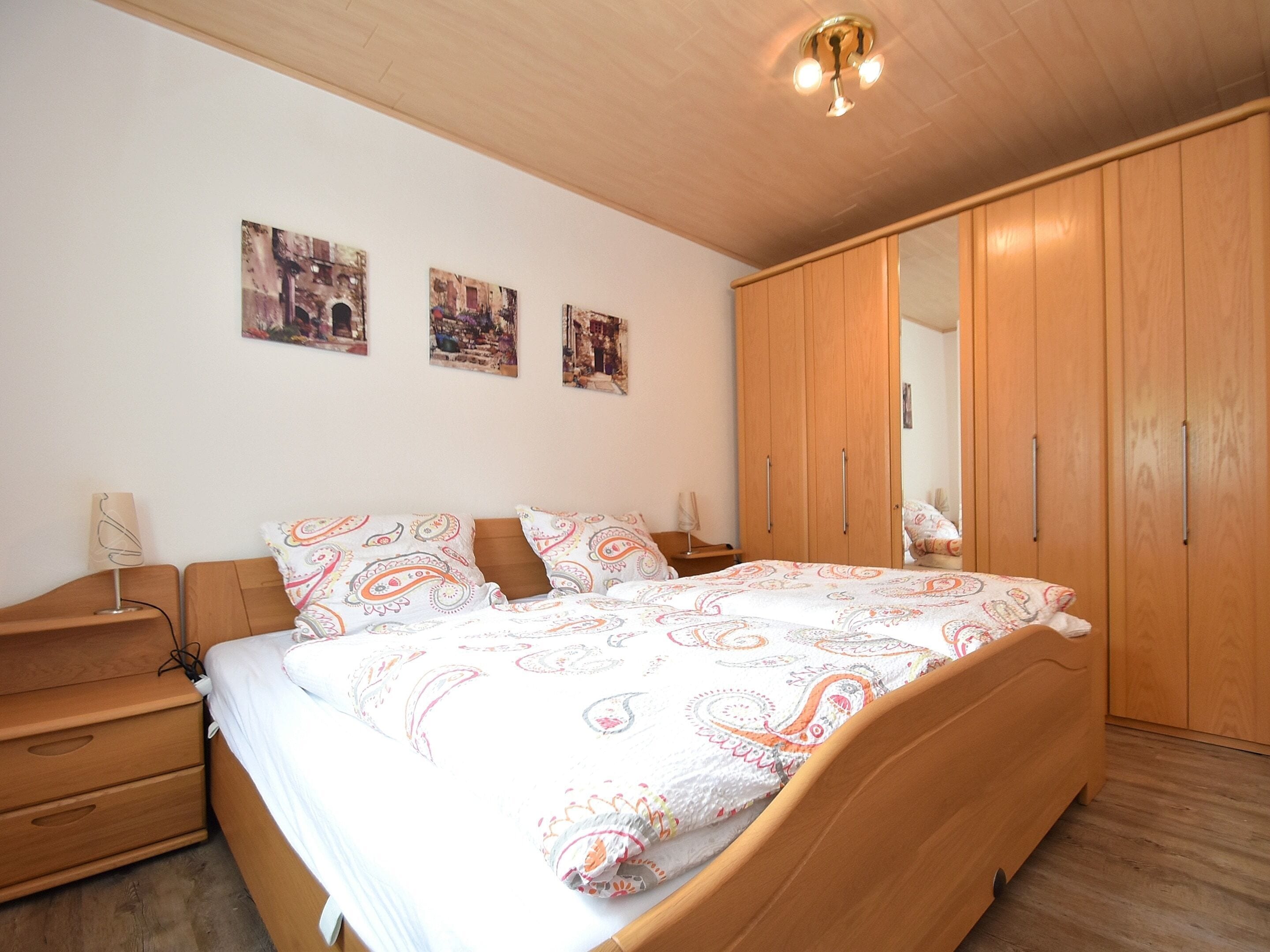 Una camera da letto con un letto in legno, un comodino, un armadio e tre quadri appesi al muro.