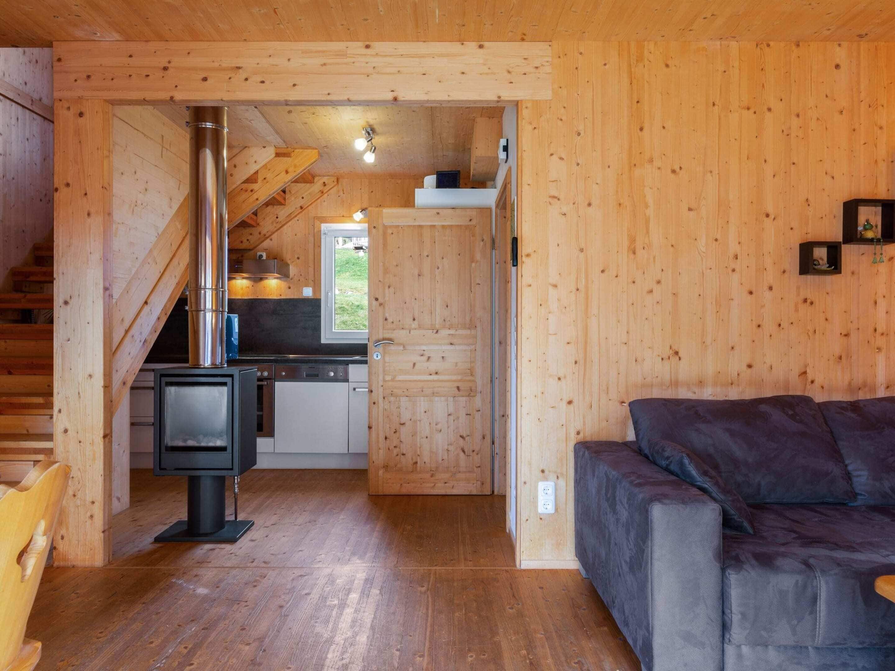 Ein gemütliches Blockhaus-Interieur mit Holzausstattung, Kamin, Küchenbereich und einer Couch.