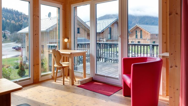 A wooden cabin with large windows, a dining table, two chairs, and a red chair. - Luxury Chalet in Hohentauern near Ski Area (Hohentauern)