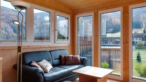 A modern living room with a leather sofa, a wooden coffee table, and large windows offering a view of a mountainous landscape. - Luxury Chalet in Hohentauern near Ski Area (Hohentauern)