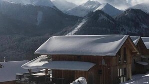 Une cabane en bois dotée d’un balcon, entourée de montagnes enneigées et surplombant un ciel dégagé.