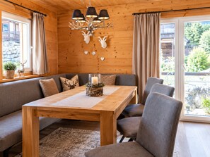 A cozy cabin interior with a wooden dining table, grey upholstered seating, and a chandelier with antler decorations. - Cozy Chalet in Hohentauern near Ski Area (Hohentauern)