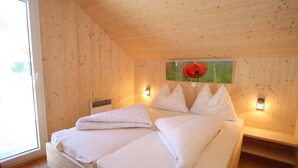 Une pièce en bois avec un lit, deux lampes fixées au mur, un radiateur et une fenêtre.